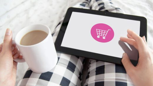 Kobieta z tabletem na kolanach lezy w łóżku i kupuje przez internet