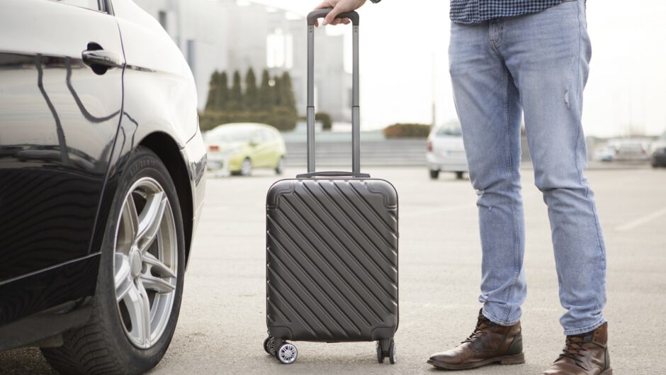 Mężczyzna stoi z walizką koło samochodu który wynajął na lotnisku