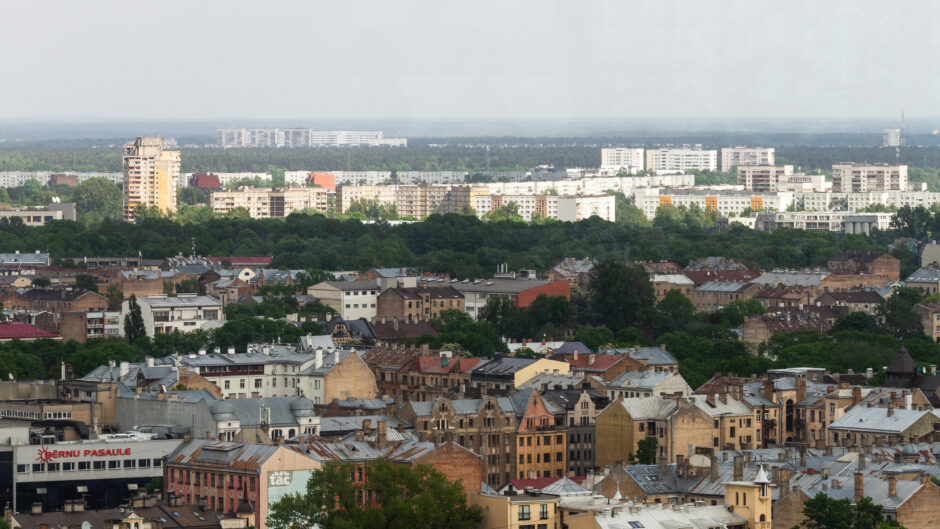 Obrazek przedstawia malowniczą panoramę Łodzi, z wieżowcami i blokami w tle. Wśród gęstej zabudowy można zauważyć zarysujące się wieżowce, które tworzą kontrast z tradycyjną architekturą miasta.