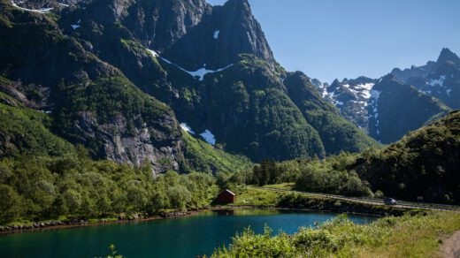 Ten ujmujący obrazek ukazuje malowniczy krajobraz Norwegii, gdzie jezioro o błękitnej tonacji rozciąga się wśród majestatycznych gór w tle. Przenikliwe szczyty górskie kontrastują z spokojną powierzchnią jeziora, tworząc scenę pełną harmonii i naturalnej piękności.