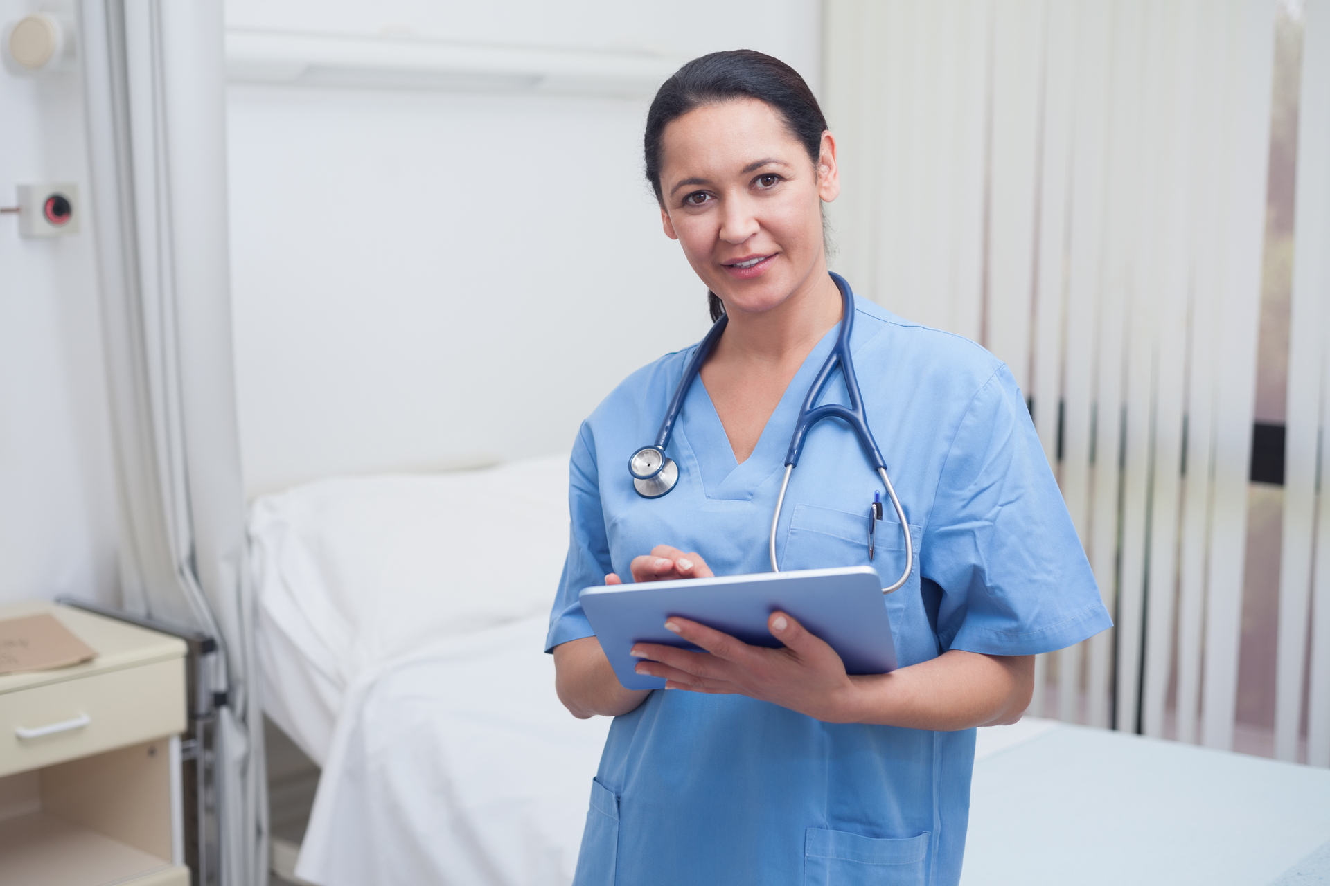 Uśmiechnięta pielęgniarka, która stoi przy łóżku pacjenta i trzyma w ręce notatnik