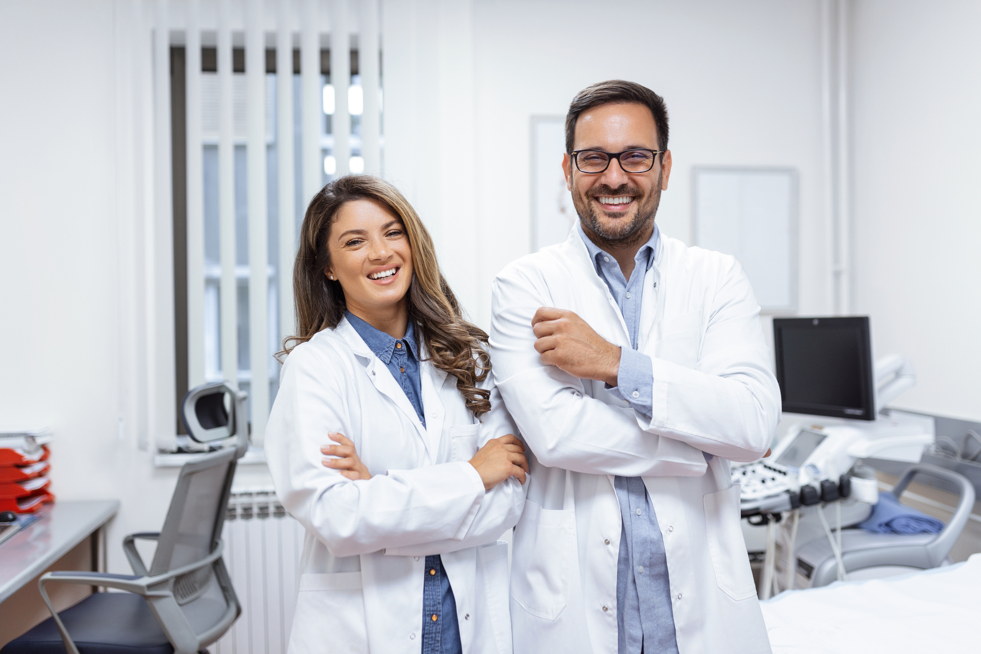 Lekarz i pielęgniarka w kitlach uśmiechający się do zdjęcia w gabinecie lekarskim