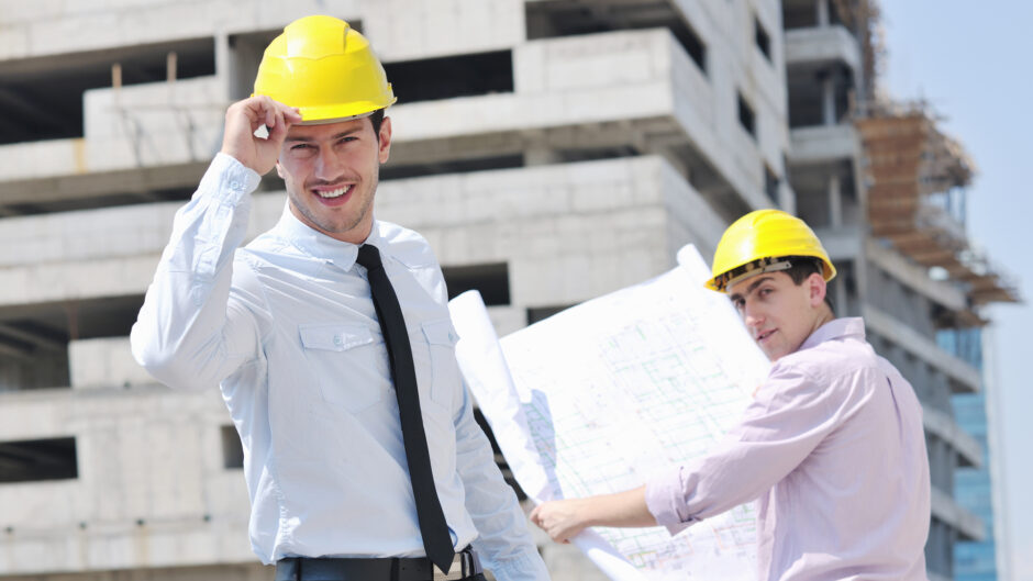 Dwóch pracowników firmy budowlanej, ubranych w ochronne kaski i białe koszule w krawatem