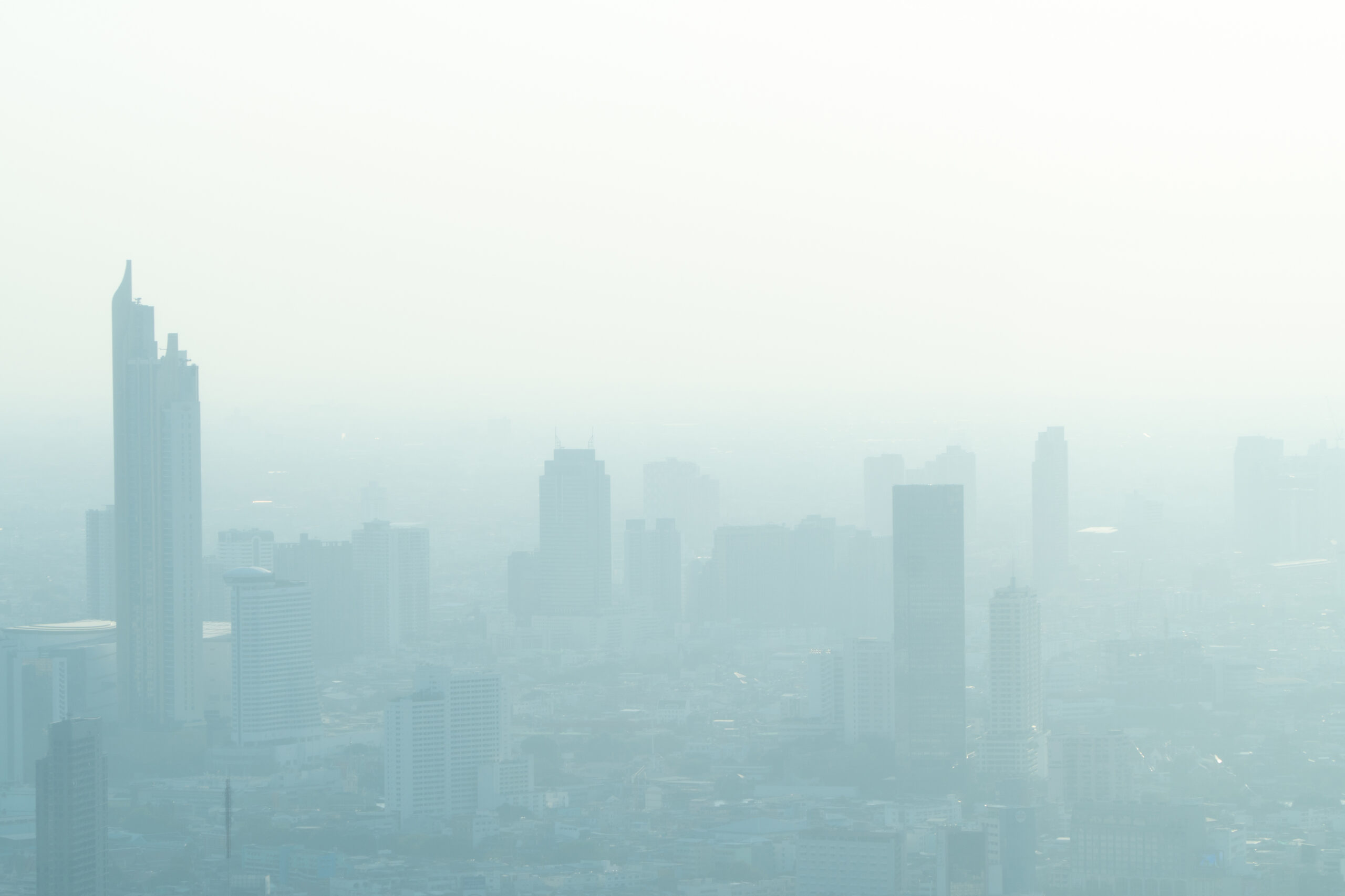 Na zdjęciu widać miasto, które jest zahamowane przez gęsty smog i mgłę, co jest wynikiem zanieczyszczenia powietrza. Widać zatłoczone ulice i budynki, z których widać jedynie ich zarys. Zdjęcie to doskonale ilustruje, jak negatywny wpływ ma zanieczyszczenie powietrza na jakość życia mieszkańców miast oraz jak ważne jest podejmowanie działań mających na celu poprawę jakości powietrza.