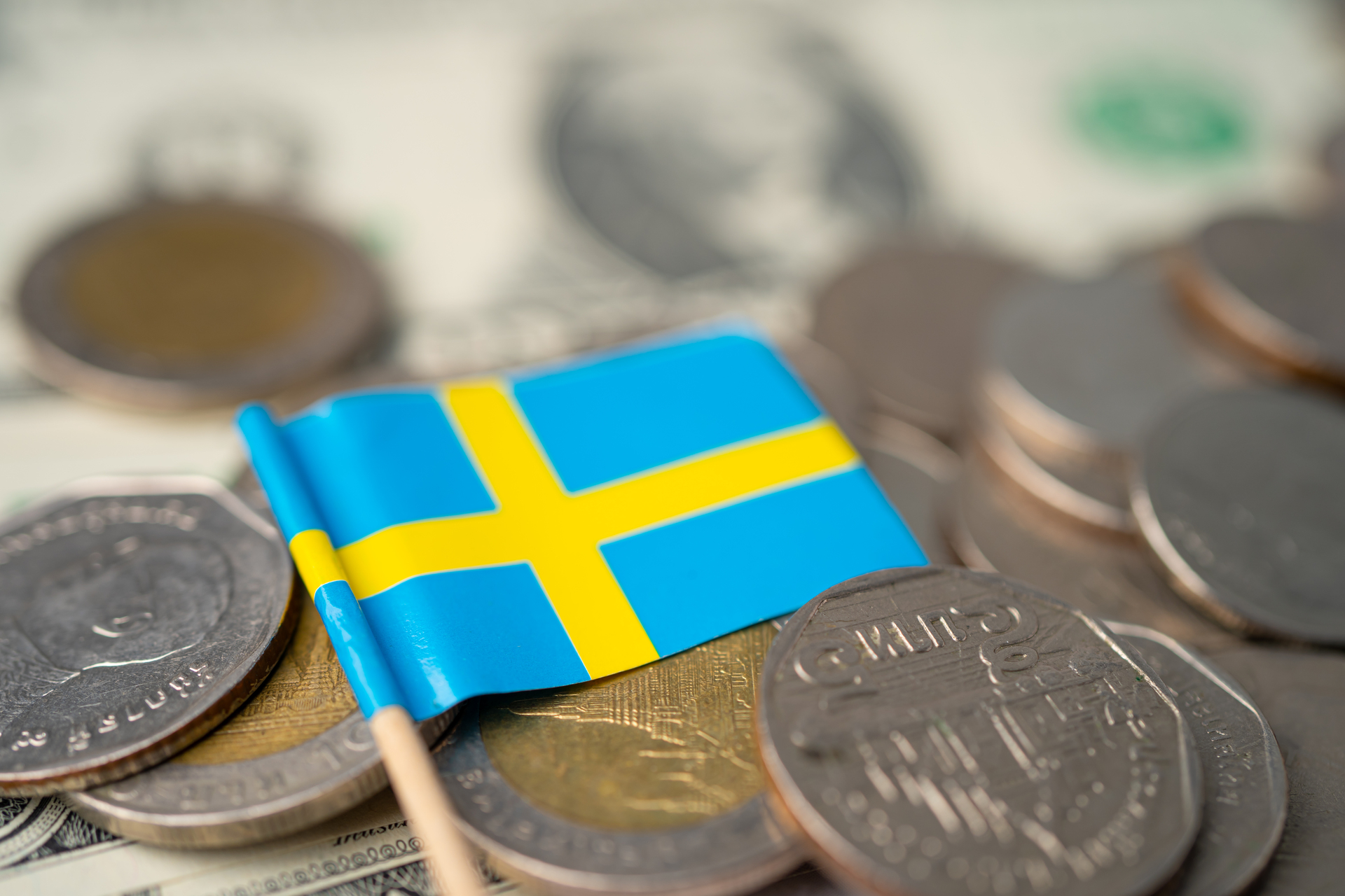 Szwedzka flaga w otoczeniu monet, które symbolizują gospodarczą siłę i stabilność Szwecji