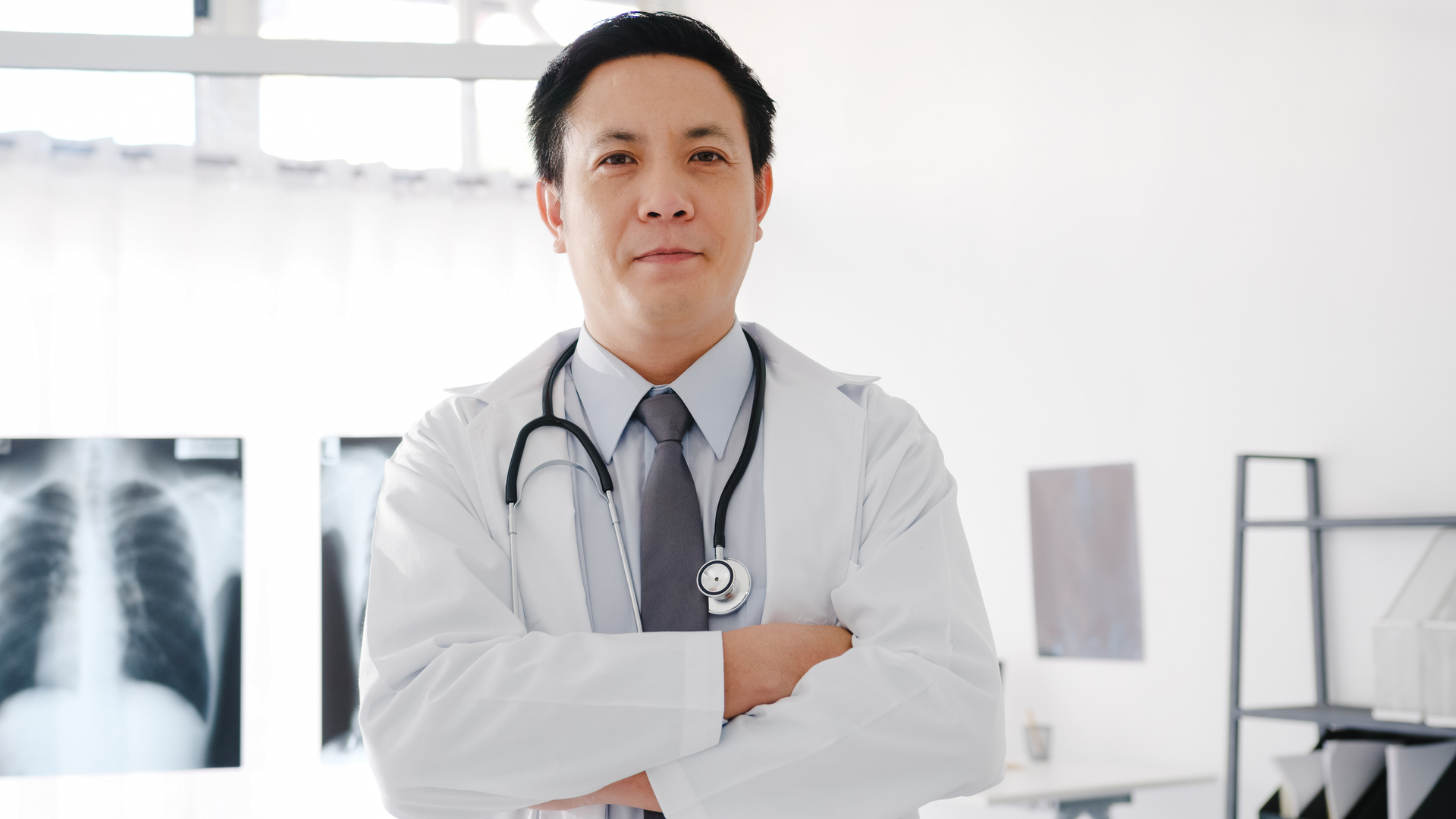 Japoński lekarz, który ubrany jest w biały fartuch medyczny i z założonymi rękami pozuje do zdjęcia