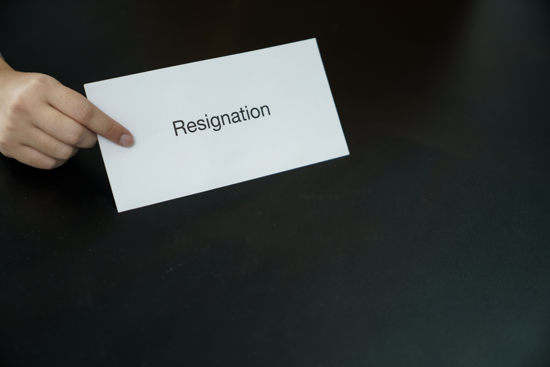 Kartka papieru z wyrazem "Resignation" (rezygnacja) wypisanym na niej na czarnym tle