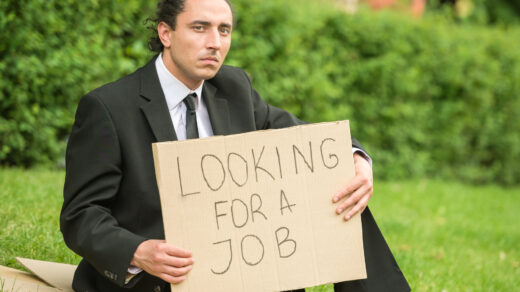 Mężczyzna trzymający tekturową tabliczkę z napisem "looking for a job" (szukam pracy)