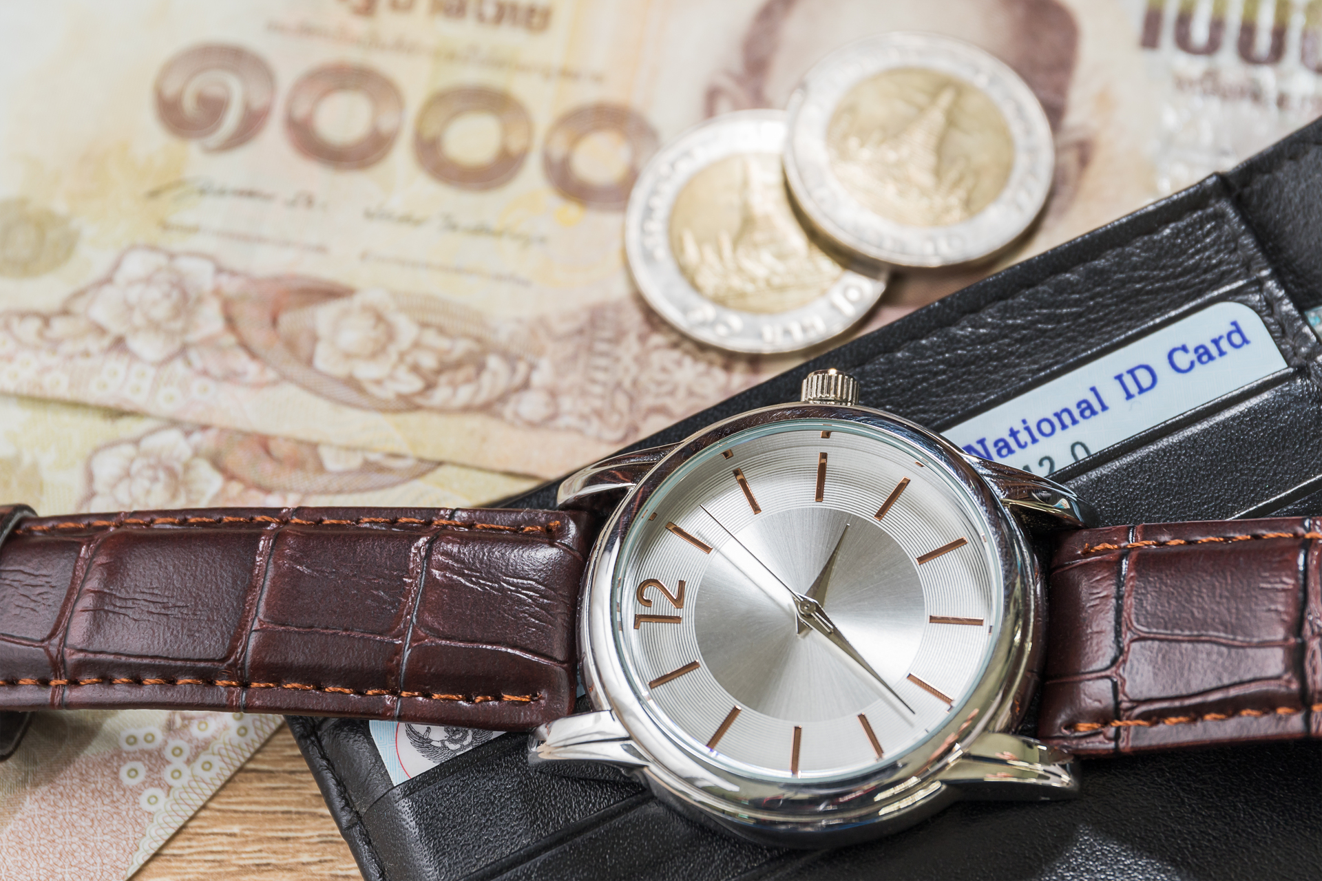 Zegarek na pasku, monety i banknoty leżące na stole