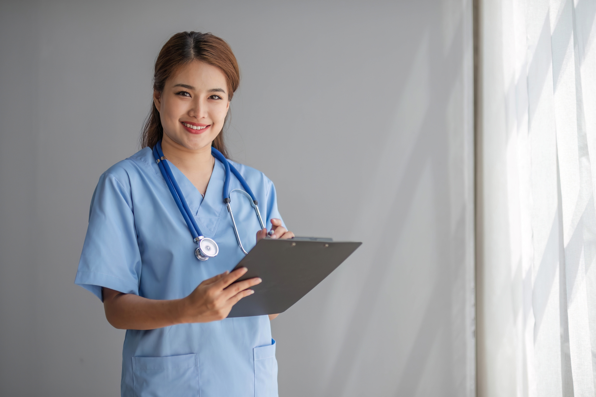 Pielęgniarka z dokumentami na tle białej ściany uśmiechająca się do zdjęcia