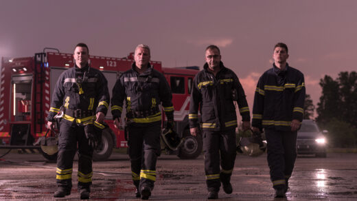 Grupa strażaków stojących na tle imponującego wozu strażackiego, gotowych do podjęcia akcji ratunkowej