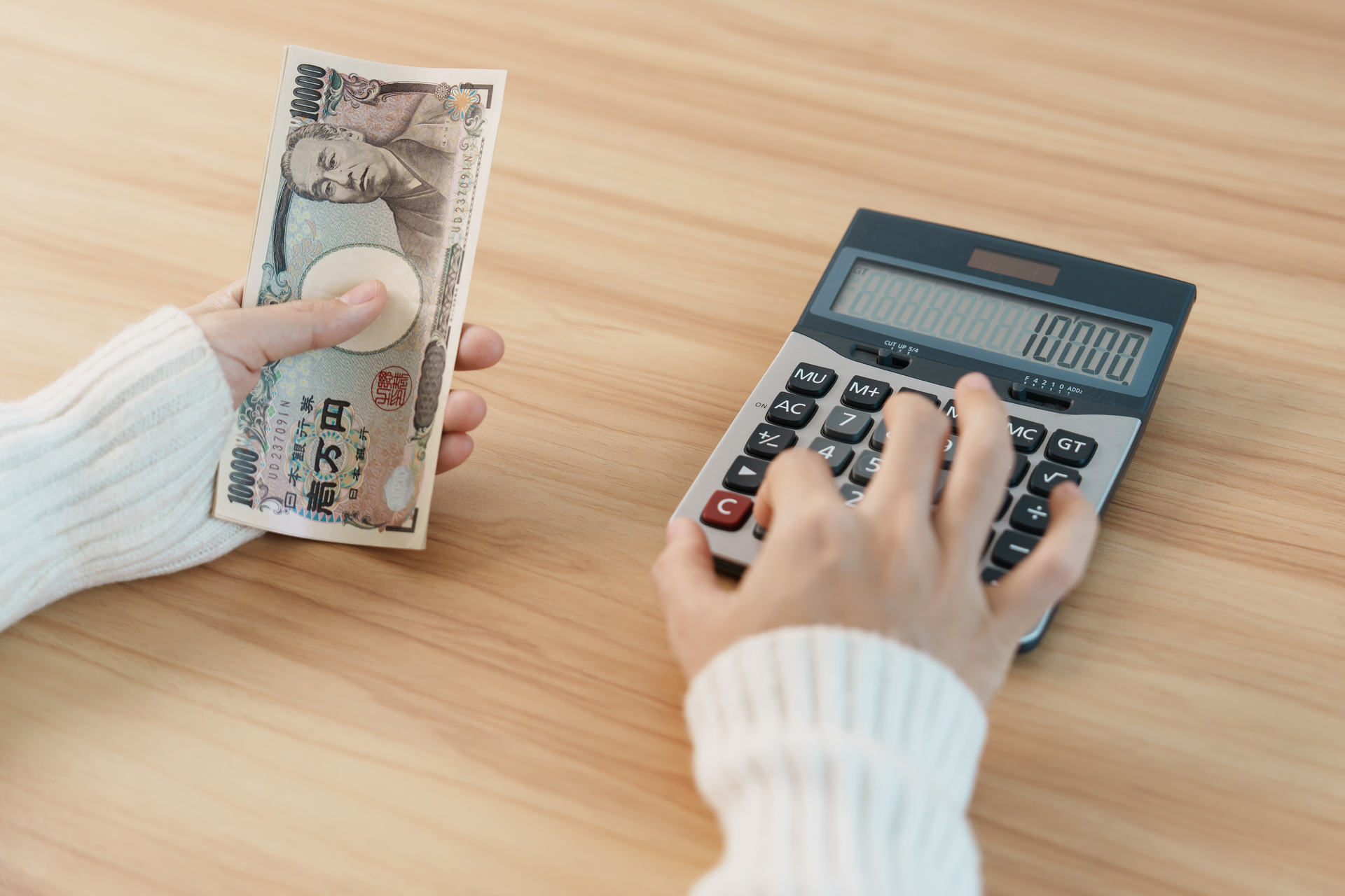 Kobieta, skupiona nad obliczaniem swojego wynagrodzenia na kalkulatorze, trzymając w rękach banknoty